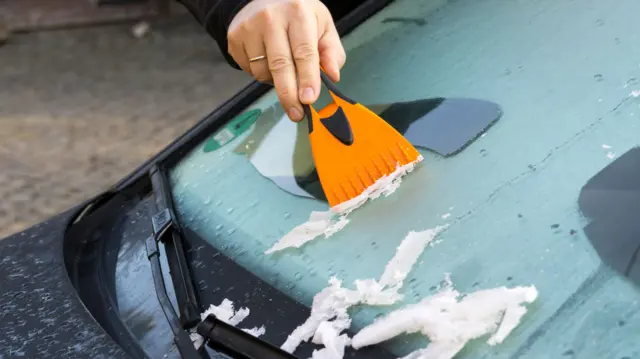 A man scrapes ice off a car windscreen