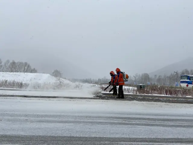 People blowing snow off paths