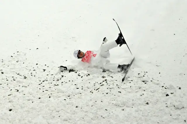 Freestyle skiier falling onto landing area with pine bits in snow