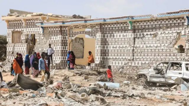 People walk next to a destroyed house and the wreckage of a car following an explosion by al-Shabab militants' during an attack on a police station on the outskirts of Mogadishu, Somalia - 16 February 2022