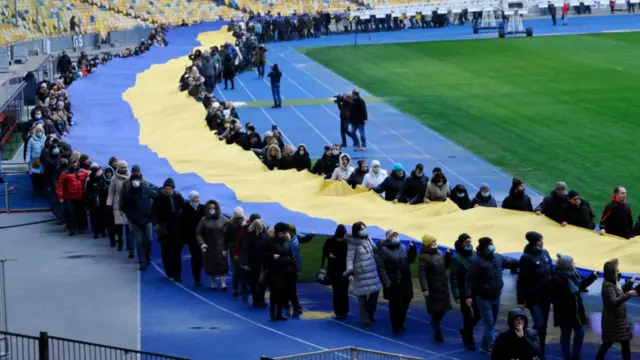 People carry a giant Ukraine's national flag at a stadium to mark a "Day of Unity" in Kyiv on February 16, 2022