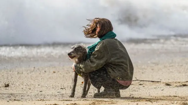 A woman and her dog windswept on a beach in Cornwall