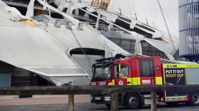 A fire engine in front of the O2 arena, which has a ripped roof