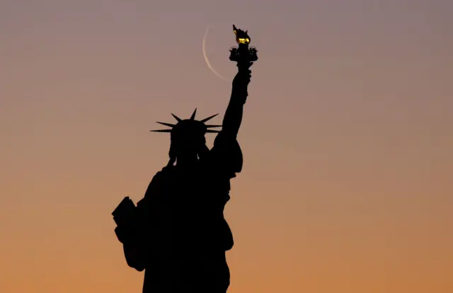 An illuminated moon rises behind the Statue of Liberty