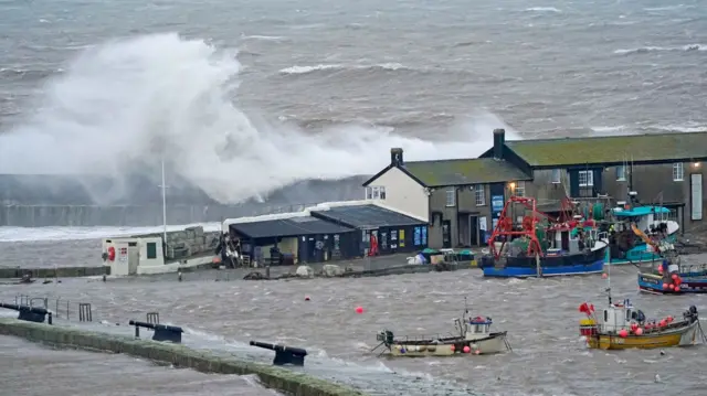 Waves crash over the sea wall at the harbour in Lyme Regis in Dorset