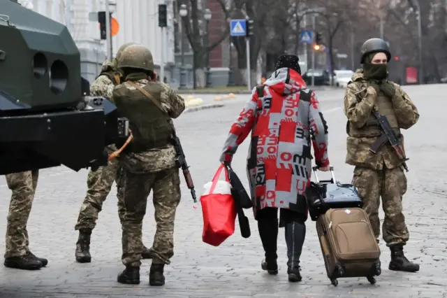 A woman walks past Ukrainian military service members guarding a road