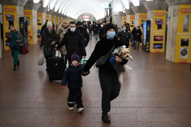 A woman holds a child's hand and carries her dog as she rushes through a metro station in Kyiv