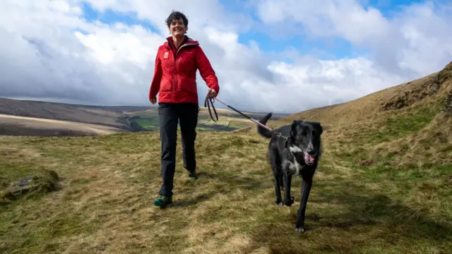 Woman walking her dog on a lead on an open landscape.