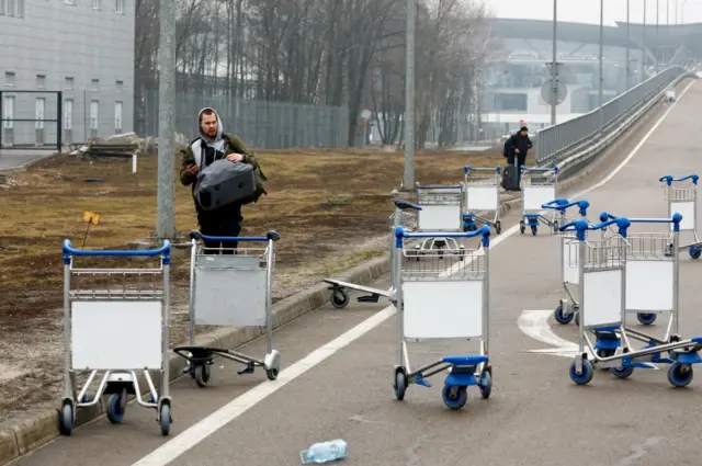 A person walks past luggage carts at Kyiv Airport after Putin authorises military operation