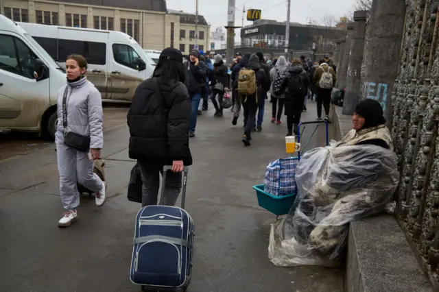 A homeless person sits outside the train station as people attempt to evacuate Kyiv