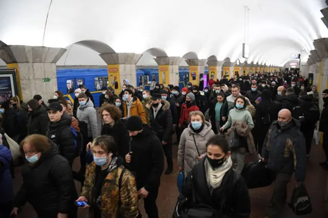 Crowds at a metro station in Kyiv as air raid sirens ring out across the city. People are carrying bags and suitcases.