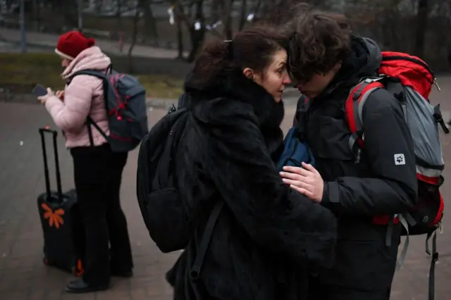 A woman speaks to a younger man, holding him close, as they stand outside a metro station in Kyiv.