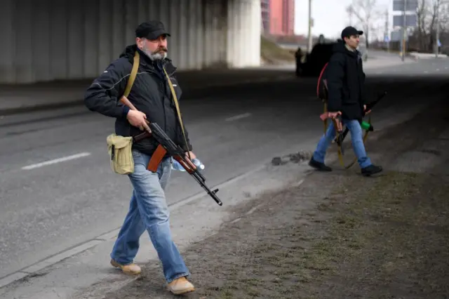 Volunteers, one holding an AK-47 rifle, protect a main road leading into Kyiv