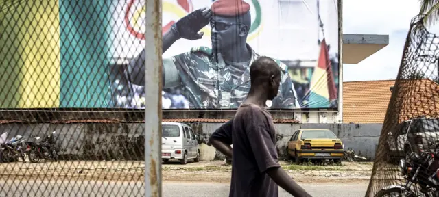 Man walking past a billboard showing Col. Doumbouya