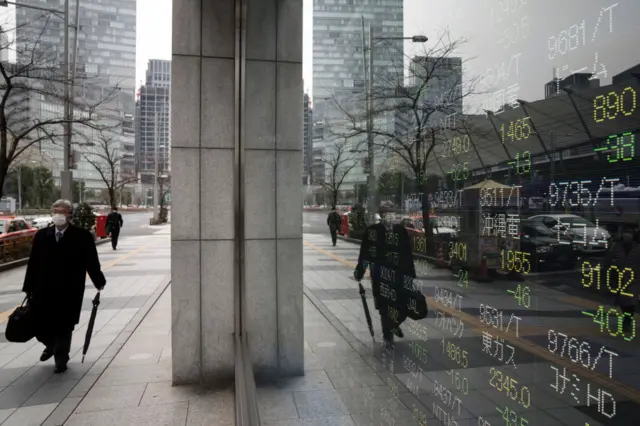 A pedestrian wearing a face mask walks past a monitor displaying stock information outside a securities firm in Tokyo, Japan.