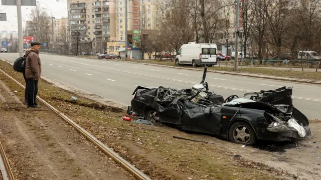 A resident of Kyiv looks at the crushed remains of a car