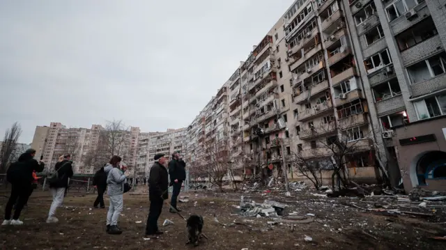 Residents look at the aftermath of overnight shelling at a residential area in Kyiv