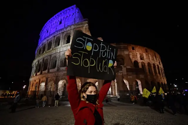 A protestor holds a banner in front of the Ancient Colosseum, as she takes part to a rally in Rome on February 25, 2022, against Russia's invasion of Ukraine