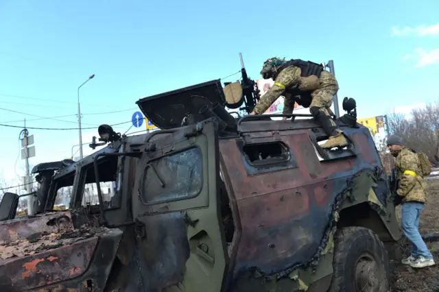 A Ukrainian fighter takes the automatic grenade launcher from a destroyed Russian infantry mobility vehicle after the fight in Kharkiv