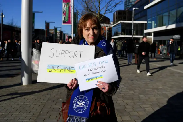 A Chelsea fan holds up signs condemning the invasion of Ukraine