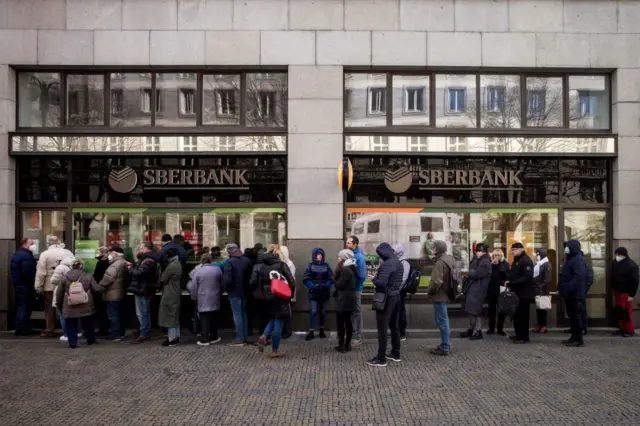 People queue outside a branch of Russian state-owned bank Sberbank to withdraw their savings and close their accounts in Prague on February 25, 2022, before Sberbank will close all its branches in the Czech Republic later in the day