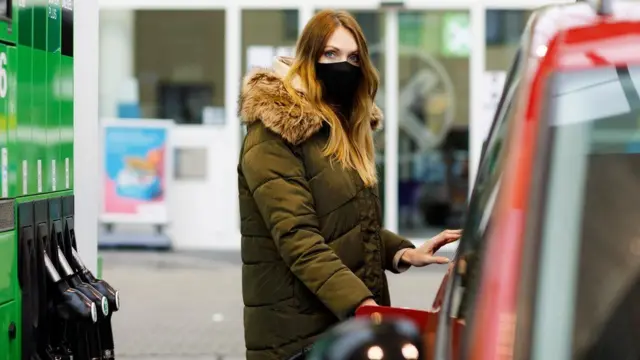 A woman puts fuel in a vehicle at a petrol station