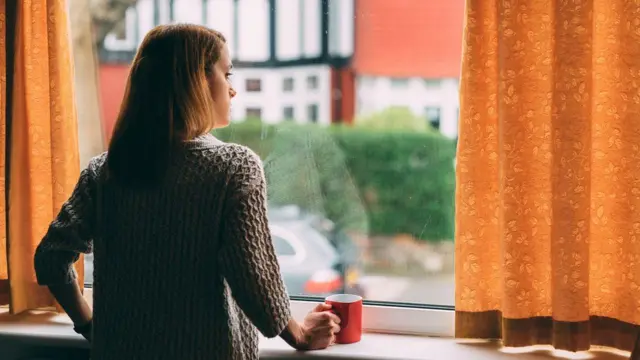 Woman at home in self isolation looking out of window