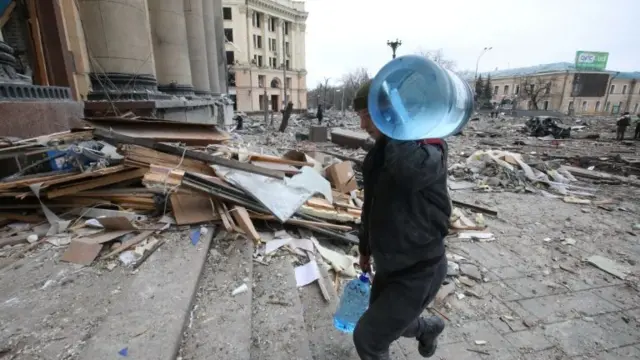 A man carries bottles of water outside the state administration office in Kharkiv after it was hit by shellfire on 1 March 2022