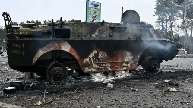 Armed man walks past a burned military vehicle on a check-point in the city of Brovary outside Kyiv on March 1, 2022.