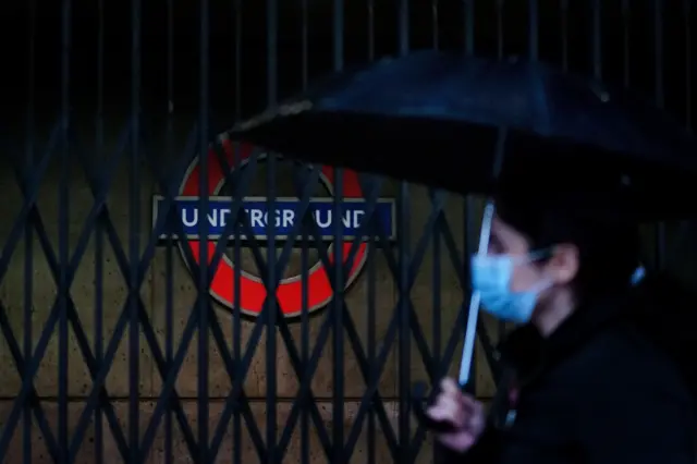 A woman holding an umbrella walks past Westminster tube station which has metal bars across the entrance