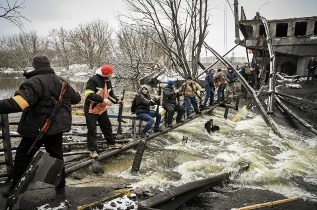 Members of a Ukrainian civil defence unit pass new assault rifles to the opposite side of a blown up bridge on Kyiv's northern front