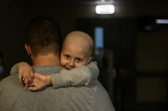 A child patient, whose leukaemia treatment is underway, hugs his father as they walk along the hallways of the basement floor