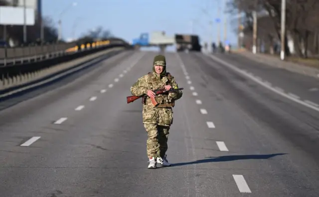 An Ukrainian service member patrol the empty road on west side of the Ukrainian capital of Kyiv