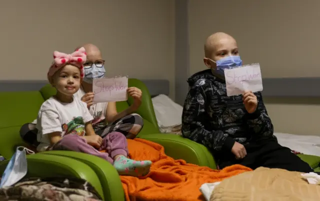 Young patients whose treatments are underway hold papers with the words "no war" written in them, at the hallways of the basement floor of the hospital