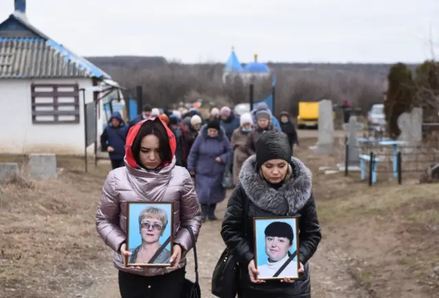 Women hold up portraits of Yelena Ivanova and Yelena Kudrik