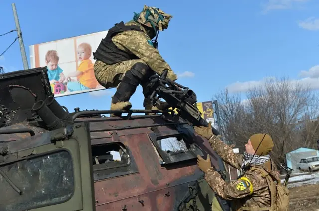 Ukrainian soldiers tear a grenade launcher from a destroyed Russian vehicle