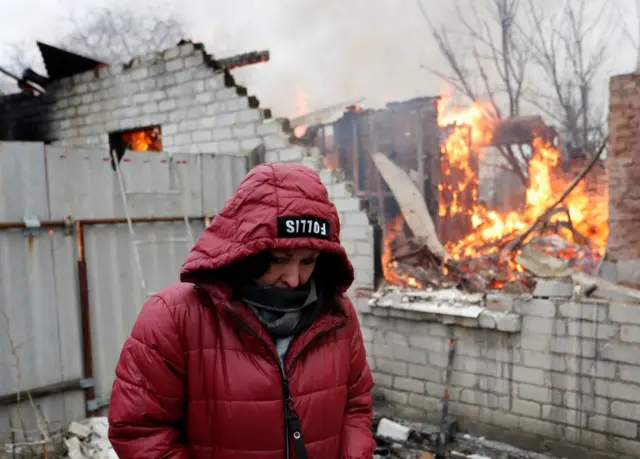 A woman standing in front of her burned home