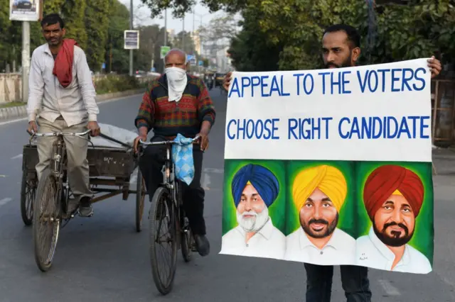 An artist holds a painting with the portrait pictures of various political party leaders, urging the public to cast their ballot, as a part of awareness campaign on the eve of Punjab state assembly elections, in Amritsar on February 19, 2022.