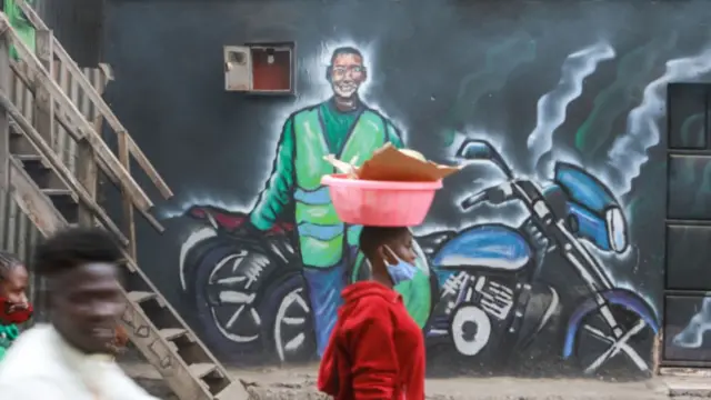 A woman wearing a face mask walks past a mural depicting a boda boda rider in Nairobi.