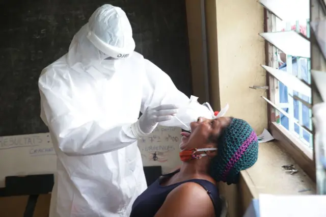 A health worker dressed in personal protective equipment (PPE) collects an oral swab from a woman during a COVID-19 coronavirus test at the Nkembo health centre in Libreville on July 9, 2020.