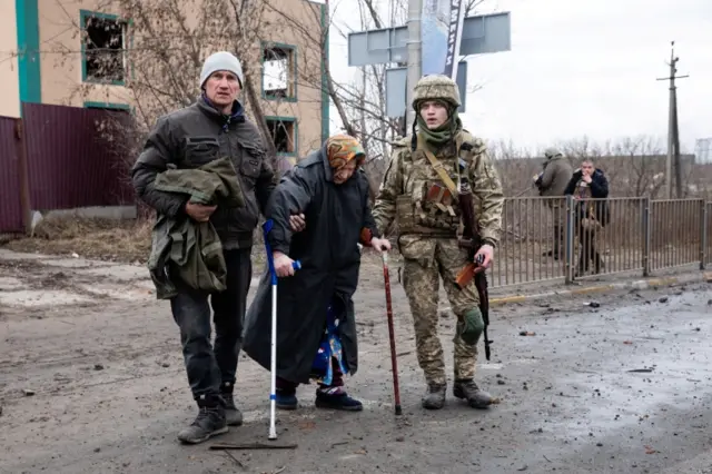 A Ukrainian service member assists an elderly woman as evacuees fleeing Ukraine-Russia conflict walk along a road in the town of Irpin in the Kyiv region