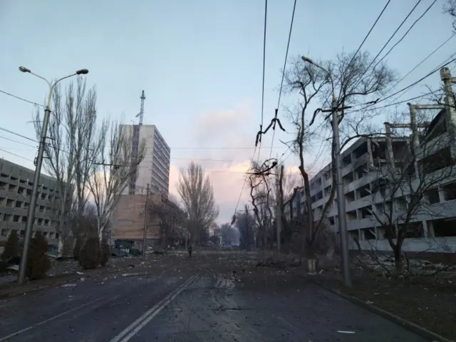 A lone person walks down a deserted street, strewn with debris in the aftermath of an attack in Mariupol