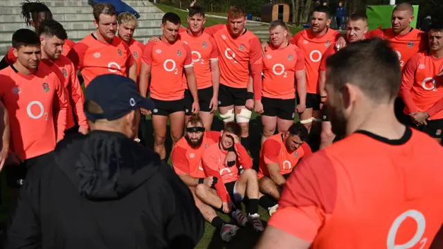 A picture of England in a huddle, with Joe Marler with his arms and legs around Harry Randall sitting on the floor