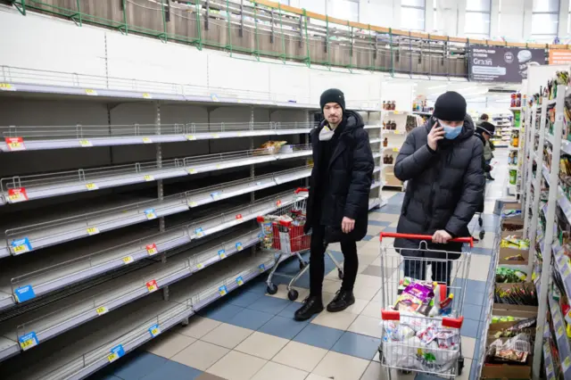 Shoppers in winter coats walk past bare aisles in a supermarket in Kyiv