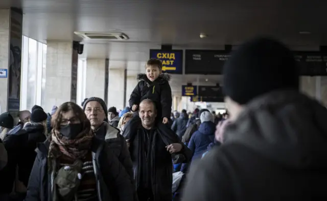 Residents crowd Kyiv's main train station seeking ways out of the capital. A dad carries a young boy on his shoulders.