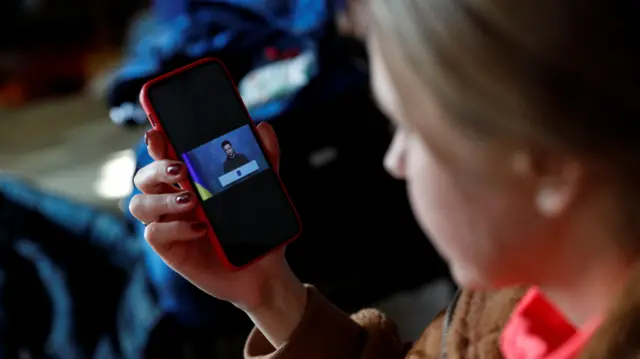 A woman from Ukraine listens to Ukrainian President Volodymyr Zelenskiy"s speech on a phone, at a refugee shelter after Russia"s invasion of Ukraine