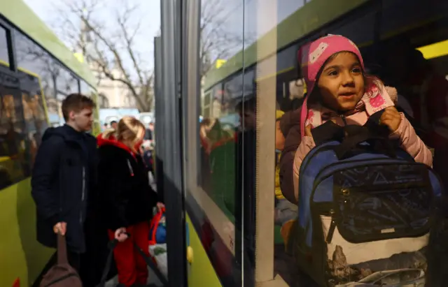 A young refugee girl smiles as she sits on a bus after fleeing the ongoing Russian invasion, outside the main train station in Lviv