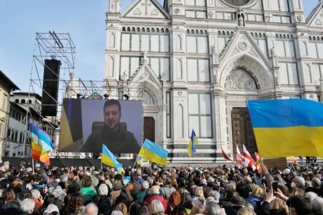 Ukrainian President Volodymyr Zelensky connects via live video link on a screen during the anti-war demonstration