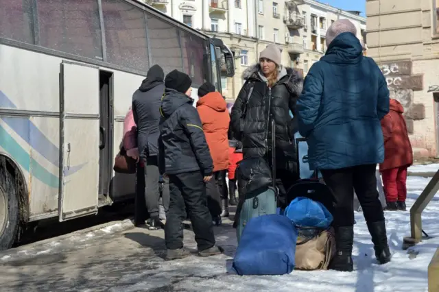 Residents stand next to a bus as they prepare to evacuate Kharkiv on March 12, 2022