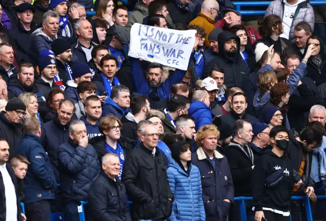 Chelse fan holds up a banner saying "It's not the fans' war" and a Ukraine flag